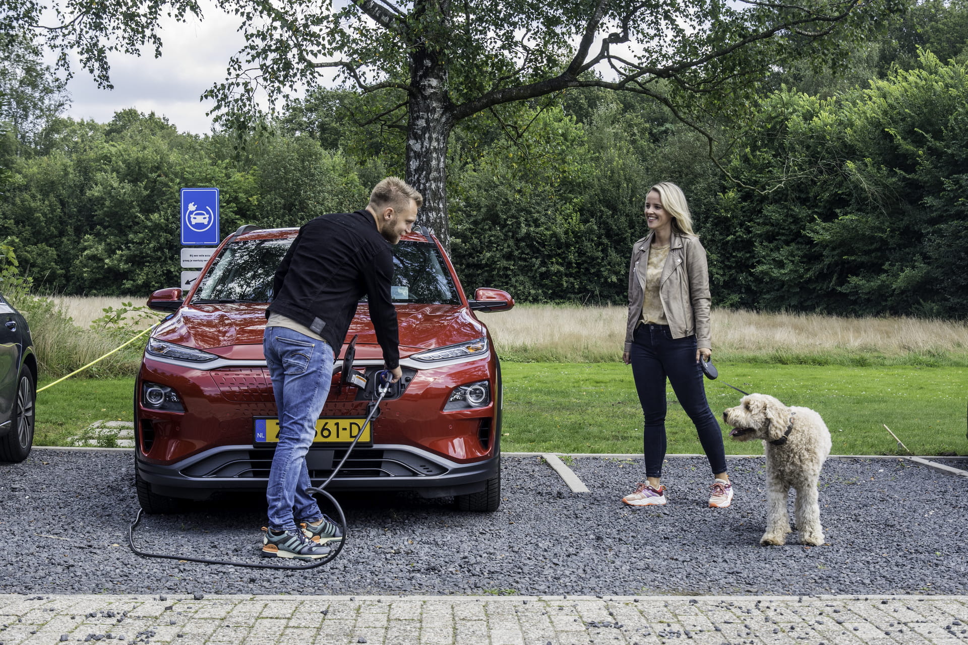 Man laadt auto op terwijl vrouw met hond erbij staat Man laadt auto op terwijl vrouw met hond erbij staat